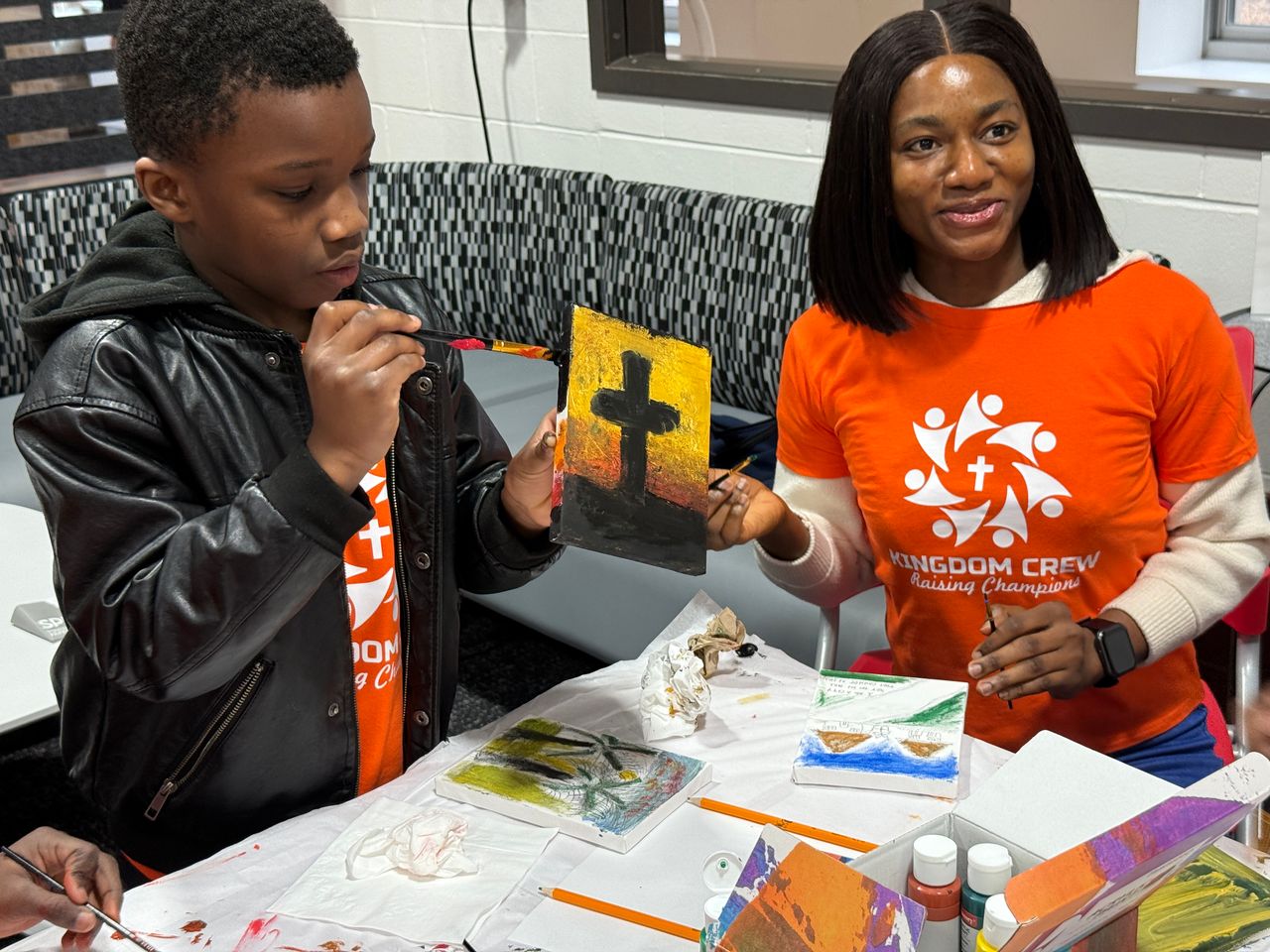 A Kingdom Crew participant painting a cross-themed canvas
